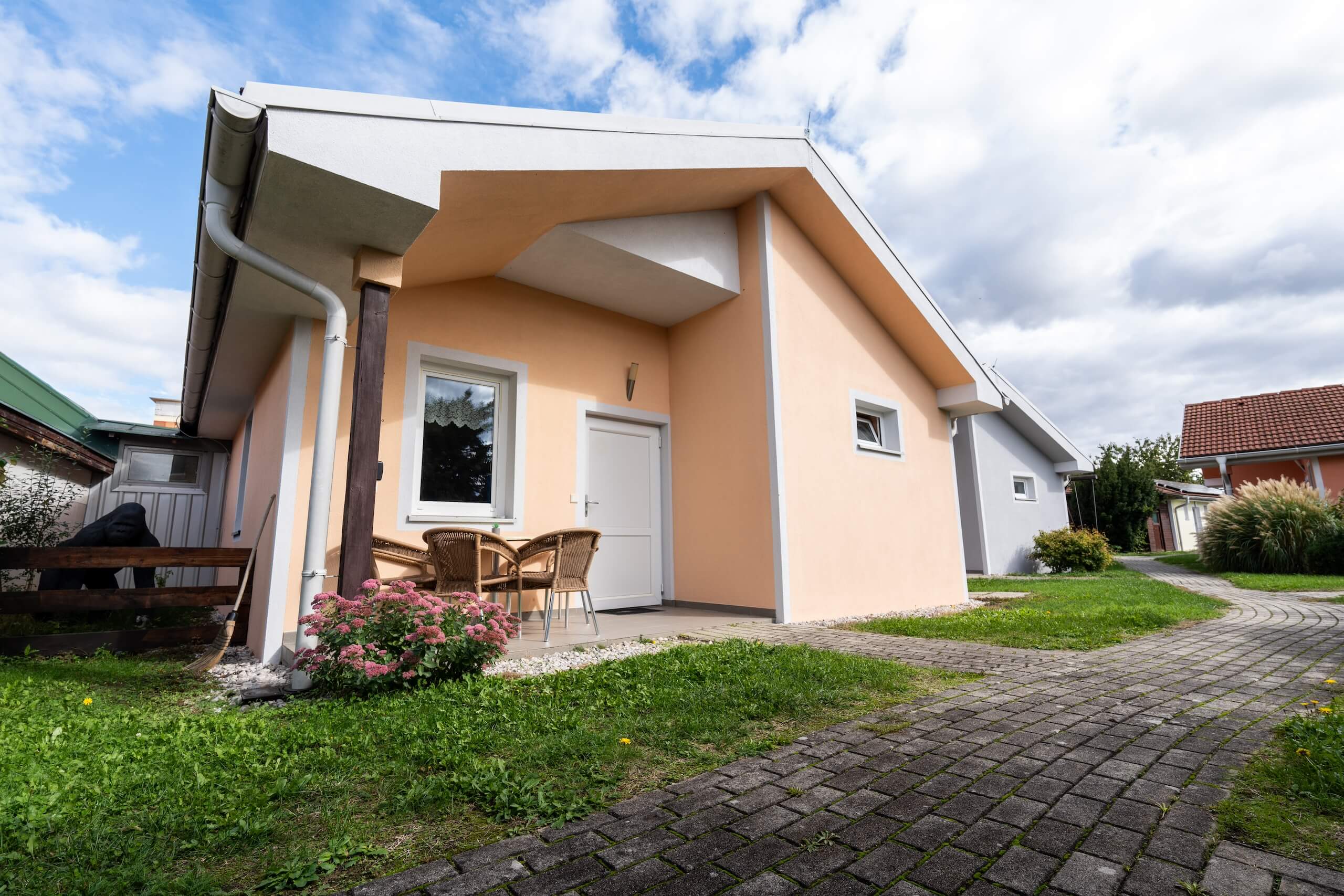 Modernes Einfamilienhaus mit Garten, blauer Himmel im Hintergrund, einladende Terrasse mit Stühlen und Blumenbeet.