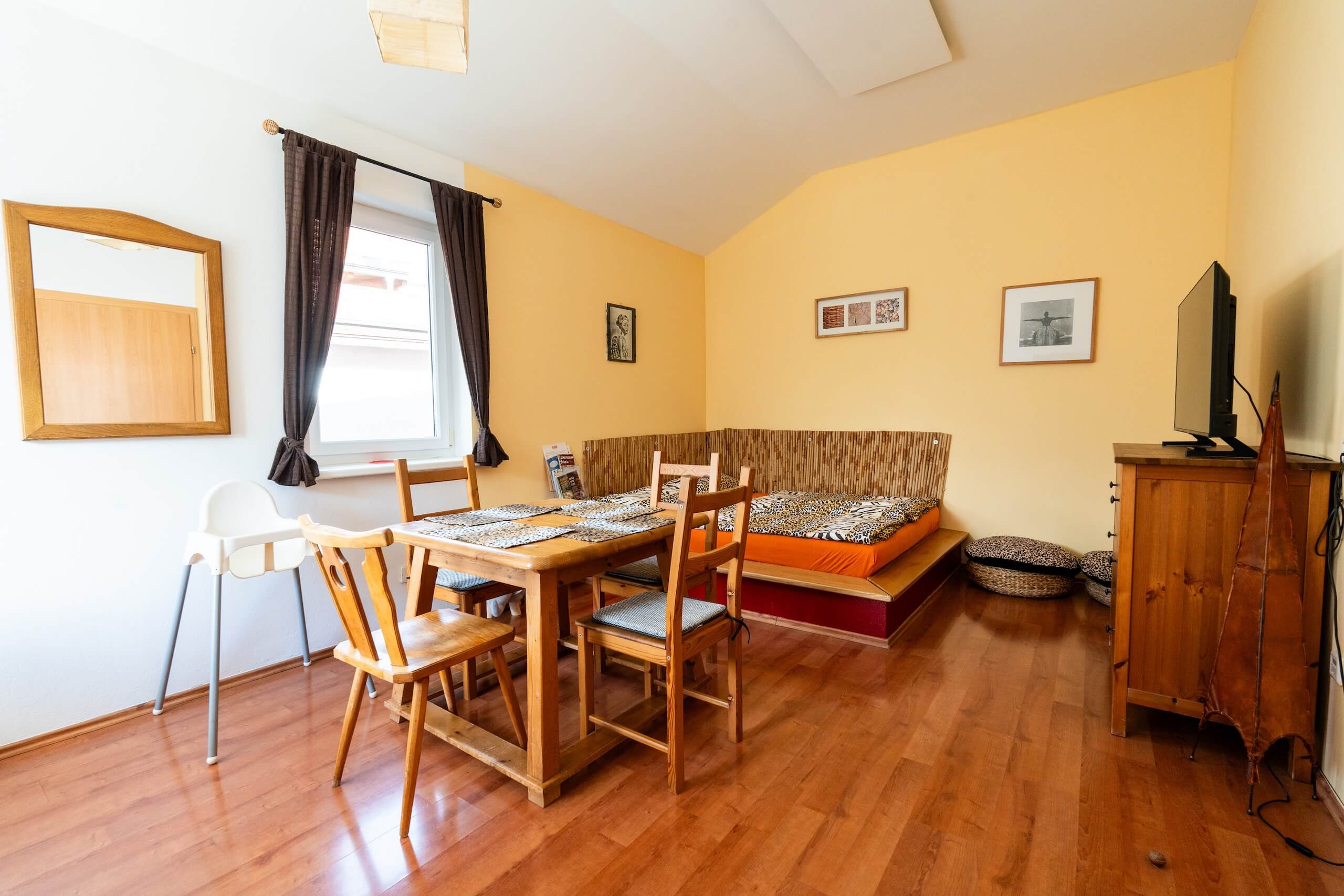 Gemütliches Wohnzimmer mit Holzmöbeln, Esstisch, TV und Ecksofa auf Laminatboden in heller, einladender Atmosphäre.